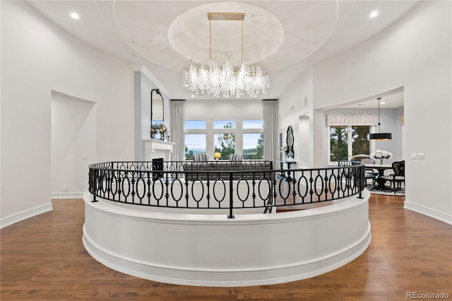 hall with a raised ceiling, hardwood / wood-style flooring, a towering ceiling, and a notable chandelier