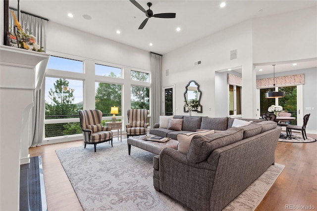 living room featuring light hardwood / wood-style flooring, ceiling fan, and a towering ceiling