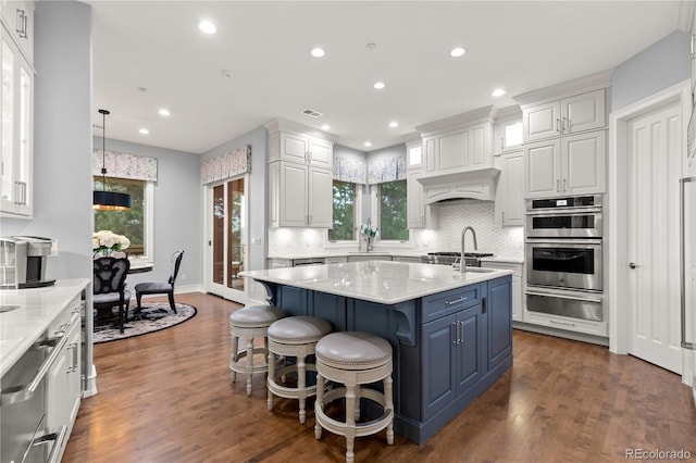 kitchen featuring backsplash, a center island with sink, dark hardwood / wood-style flooring, and double oven