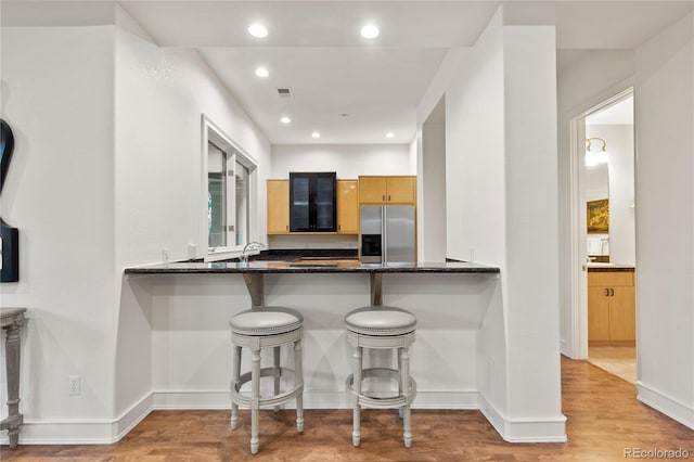 kitchen with dark stone countertops, kitchen peninsula, light wood-type flooring, and stainless steel fridge with ice dispenser