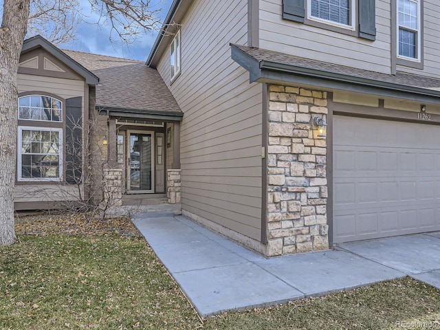 doorway to property with an attached garage, stone siding, and a shingled roof