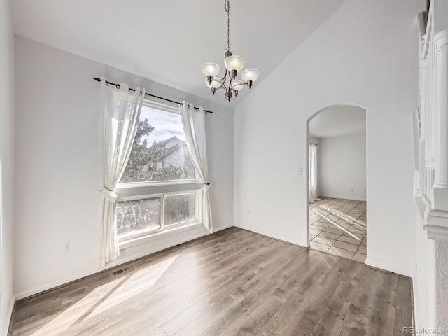 unfurnished dining area with hardwood / wood-style floors, high vaulted ceiling, and a chandelier