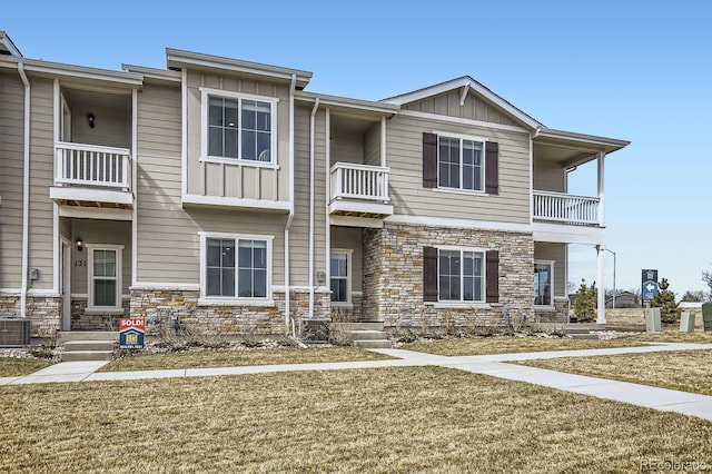 view of property featuring a front lawn, cooling unit, board and batten siding, and stone siding