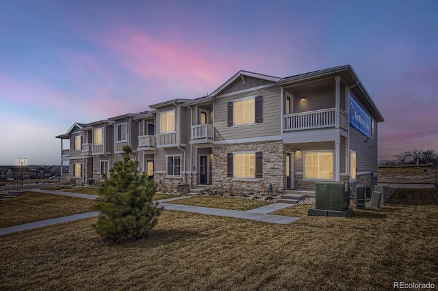 view of front facade featuring a balcony, a yard, and stone siding