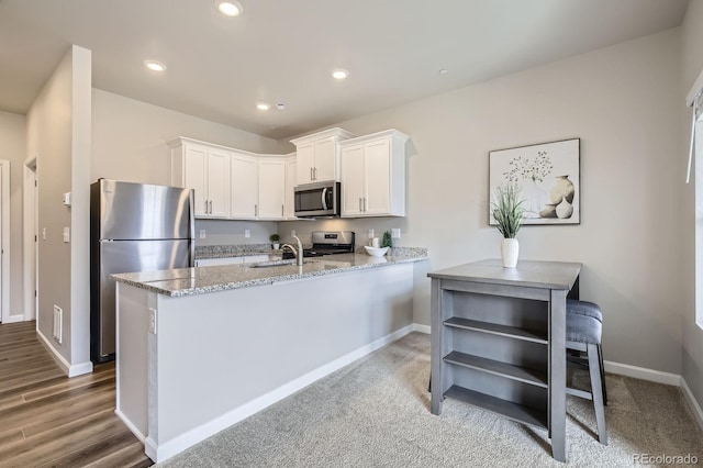 kitchen featuring light stone countertops, a peninsula, recessed lighting, appliances with stainless steel finishes, and white cabinetry