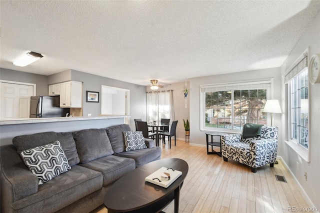 living room with a textured ceiling, light hardwood / wood-style flooring, and ceiling fan