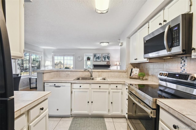 kitchen featuring sink, stainless steel appliances, light tile patterned floors, kitchen peninsula, and white cabinets