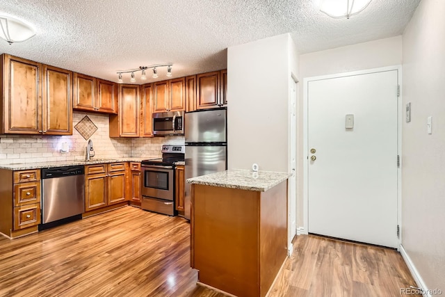 350 S Clinton St Unit 9B, Denver, CO 80247 - kitchen featuring appliances with stainless steel finishes, brown cabinets, light wood-style floors, a textured ceiling, and backsplash