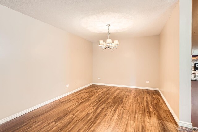 350 S Clinton St Unit 9B, Denver, CO 80247 - spare room featuring wood finished floors, a chandelier, and a textured ceiling