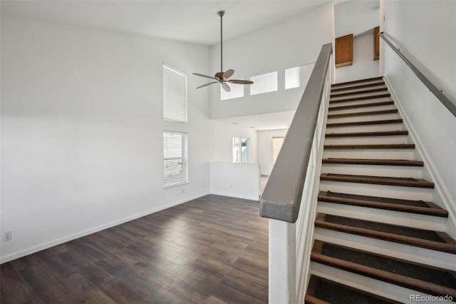 stairway with ceiling fan, baseboards, wood finished floors, and a towering ceiling