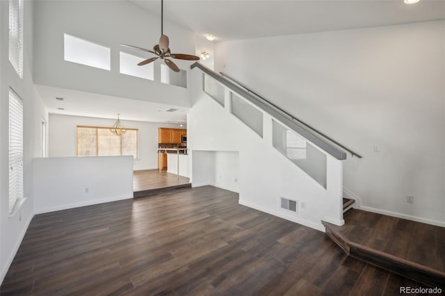 unfurnished living room featuring visible vents, ceiling fan, stairs, a high ceiling, and dark wood-style floors