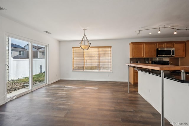 kitchen with baseboards, visible vents, dark wood finished floors, stainless steel microwave, and brown cabinets