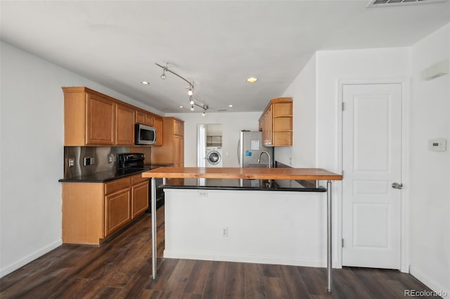 kitchen with baseboards, a peninsula, washer / clothes dryer, stainless steel appliances, and dark wood-type flooring