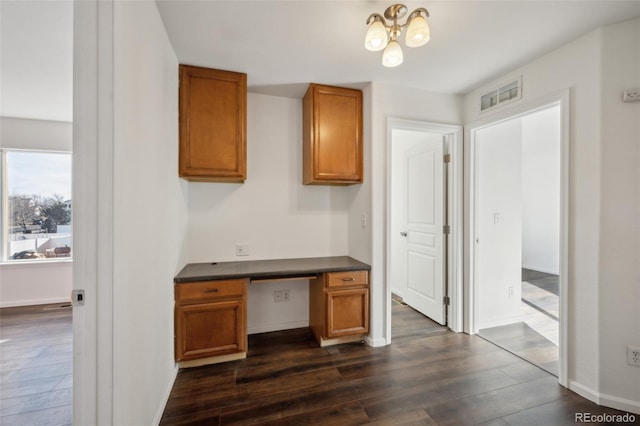 unfurnished office with visible vents, baseboards, dark wood-type flooring, and built in desk