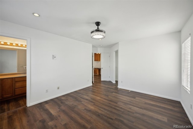 unfurnished bedroom with visible vents, baseboards, dark wood finished floors, and ensuite bathroom