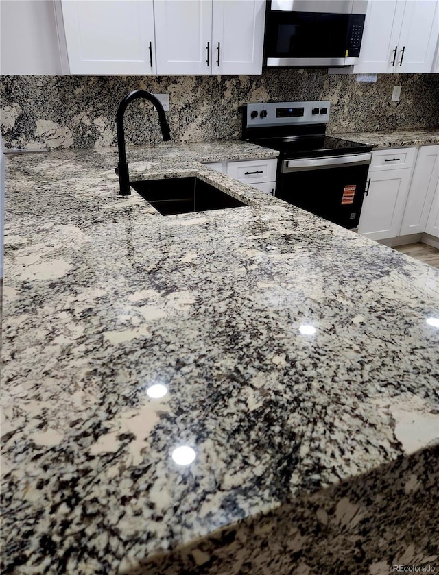 16800 E Bails Pl, Aurora, CO 80017 - kitchen with stainless steel microwave, electric stove, light stone countertops, decorative backsplash, and white cabinetry