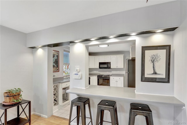 kitchen featuring kitchen peninsula, stainless steel fridge, range with electric cooktop, light wood-type flooring, and white cabinets