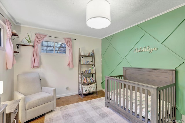 bedroom featuring a textured ceiling, light hardwood / wood-style flooring, a nursery area, and ornamental molding