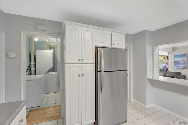 kitchen with stainless steel refrigerator, white cabinetry, light tile patterned floors, and washer and dryer