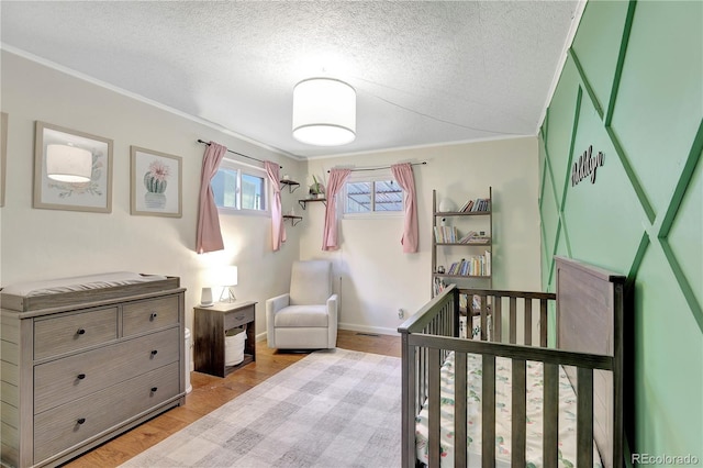 bedroom with a textured ceiling, ornamental molding, a crib, and light wood-type flooring