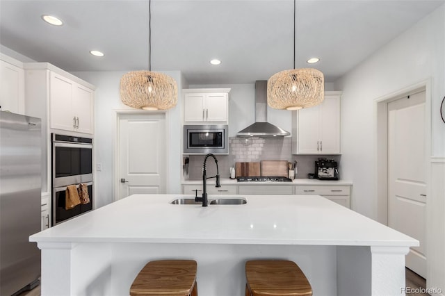kitchen featuring stainless steel appliances, wall chimney exhaust hood, a sink, light countertops, and white cabinets