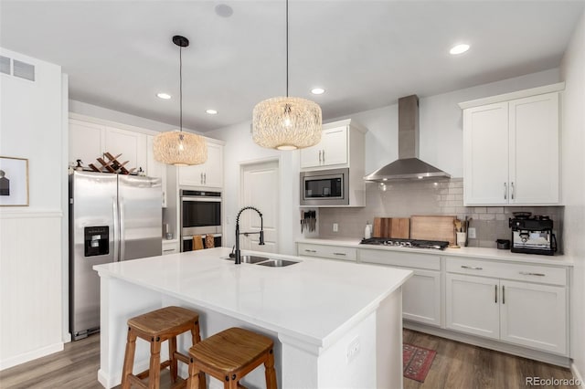 kitchen featuring wall chimney range hood, a sink, stainless steel appliances, wood finished floors, and white cabinetry