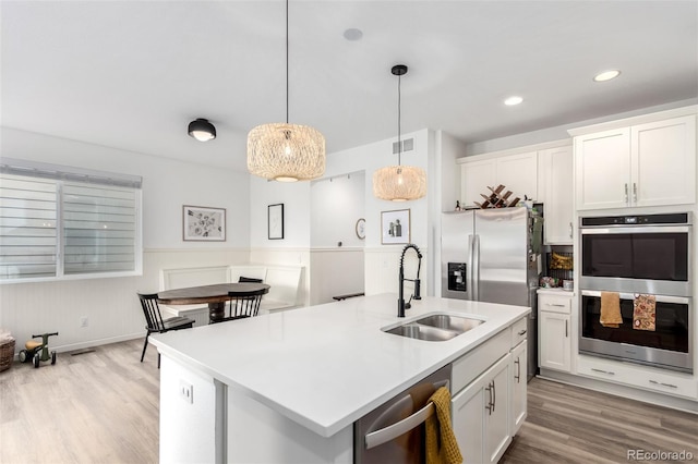 kitchen featuring double oven, a sink, light wood-style floors, light countertops, and a wainscoted wall