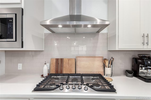 kitchen featuring wall chimney range hood, appliances with stainless steel finishes, backsplash, white cabinets, and light countertops