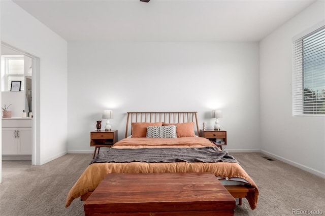 bedroom featuring light carpet, multiple windows, ensuite bathroom, and baseboards