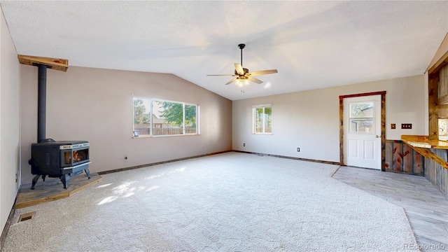 321 Stockton Ct, Gilcrest, CO 80623 - unfurnished living room featuring a ceiling fan, lofted ceiling, baseboards, a wood stove, and light colored carpet
