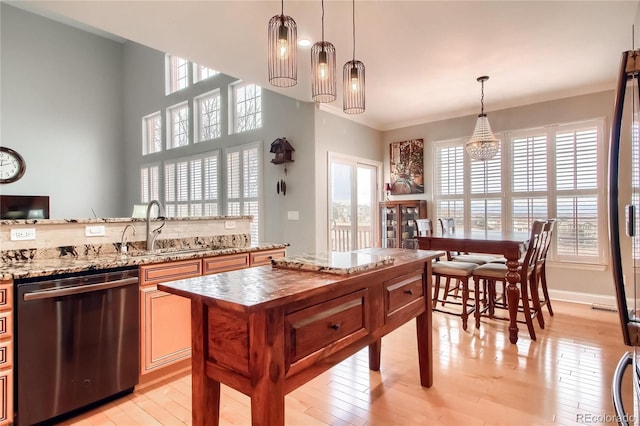 kitchen featuring sink, light hardwood / wood-style flooring, light stone counters, decorative light fixtures, and stainless steel dishwasher