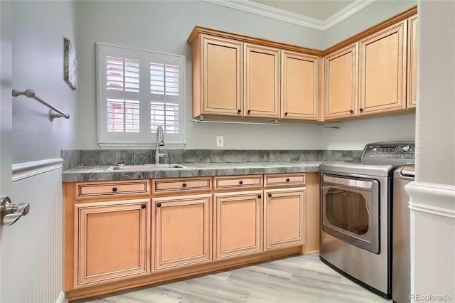 laundry room featuring sink, cabinets, washing machine and clothes dryer, crown molding, and light wood-type flooring