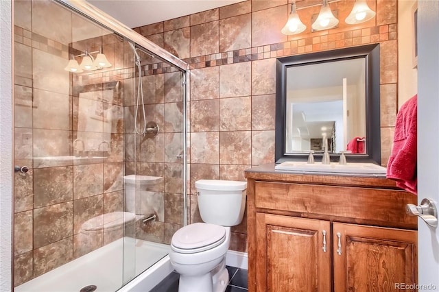 bathroom with vanity, toilet, a shower with shower door, and tile walls