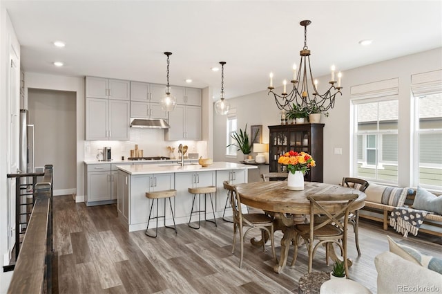 kitchen with backsplash, gray cabinets, pendant lighting, dark wood-type flooring, and a kitchen island with sink