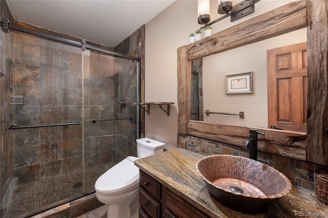 bathroom with toilet, a shower stall, vanity, and a textured ceiling