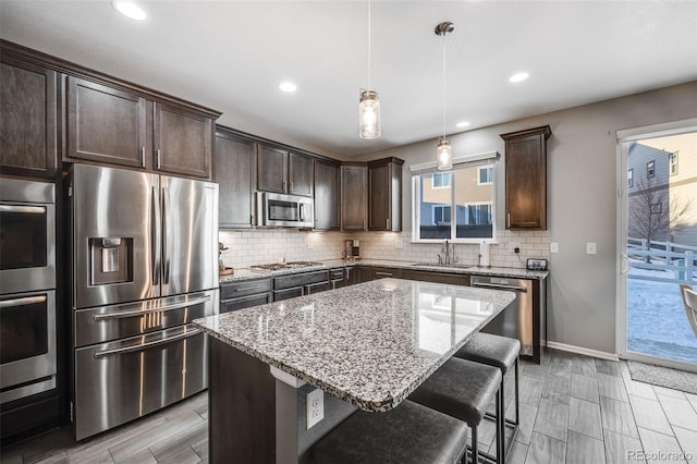 kitchen with stainless steel appliances, sink, a center island, light stone counters, and hanging light fixtures