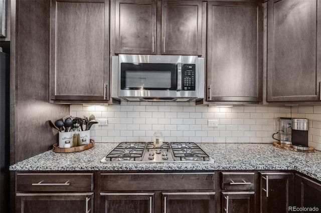 kitchen with light stone countertops, dark brown cabinetry, tasteful backsplash, and appliances with stainless steel finishes