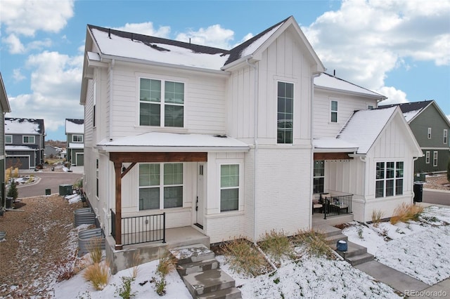 snow covered rear of property featuring covered porch