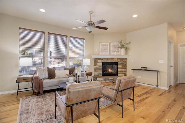 living room featuring ceiling fan, a stone fireplace, and light hardwood / wood-style flooring