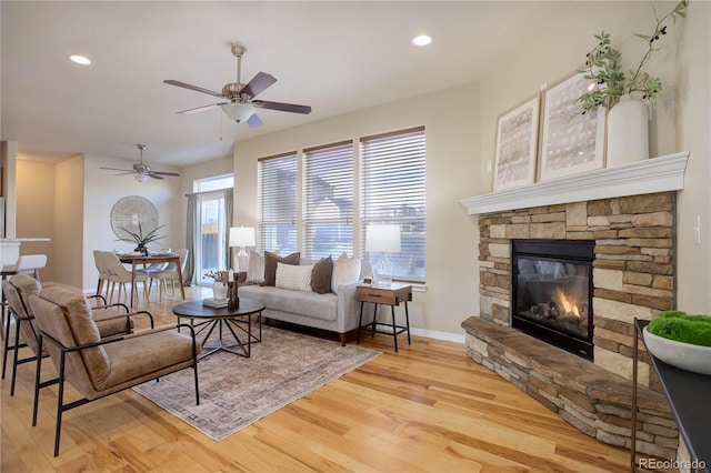 living room featuring ceiling fan, light hardwood / wood-style floors, and a stone fireplace