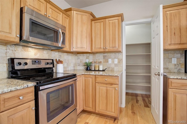 kitchen featuring decorative backsplash, light stone counters, light hardwood / wood-style flooring, and appliances with stainless steel finishes