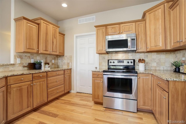 kitchen with light stone countertops, appliances with stainless steel finishes, backsplash, and light hardwood / wood-style floors