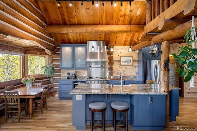 kitchen with light stone counters, sink, hanging light fixtures, and wall chimney range hood