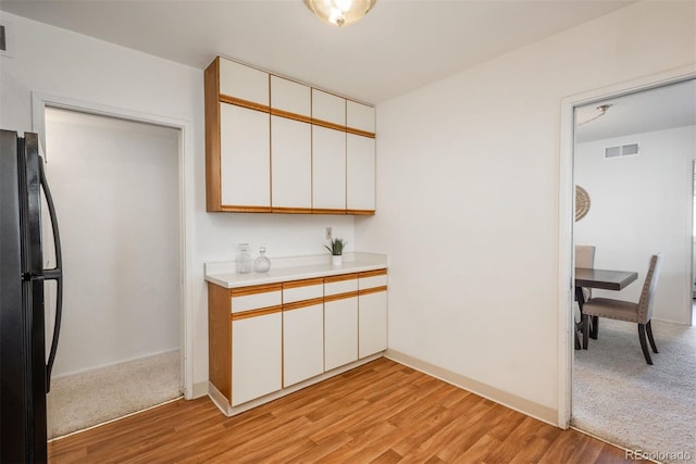 kitchen with light countertops, white cabinets, freestanding refrigerator, and visible vents
