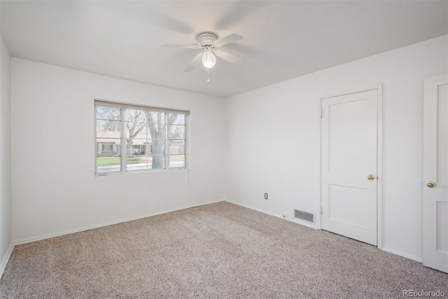 empty room with carpet floors, ceiling fan, baseboards, and visible vents