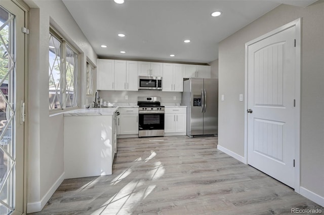 kitchen with white cabinetry, light wood-type flooring, a wealth of natural light, and appliances with stainless steel finishes