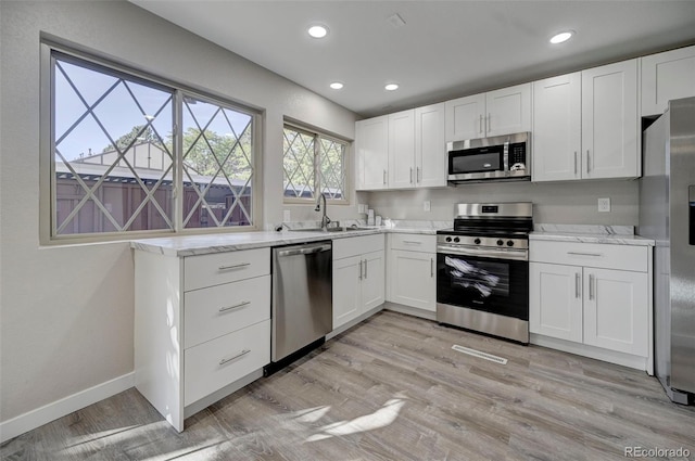 kitchen featuring appliances with stainless steel finishes, white cabinets, light stone counters, and light hardwood / wood-style floors