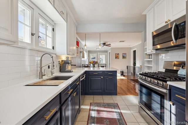 kitchen featuring appliances with stainless steel finishes, blue cabinets, white cabinets, decorative backsplash, and light tile patterned floors