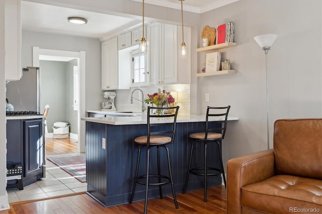 kitchen with pendant lighting, stainless steel refrigerator, white cabinets, a kitchen bar, and light hardwood / wood-style flooring