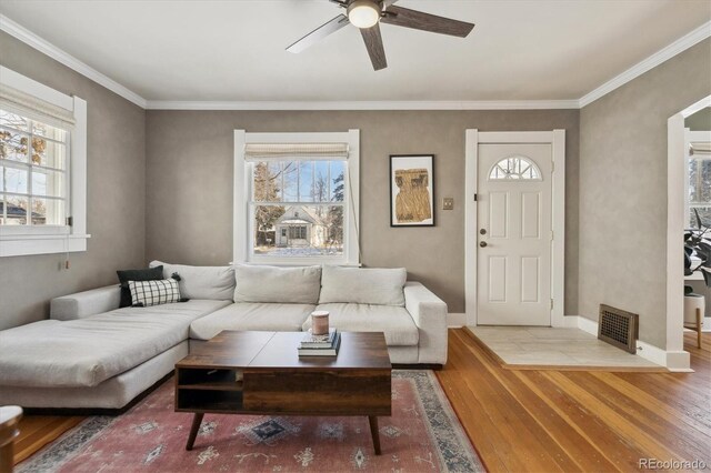 living area with baseboards, a ceiling fan, wood finished floors, and crown molding